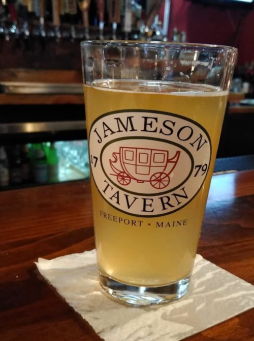 A glass of beer with a logo for Jameson Tavern in Freeport, Maine, sitting on a bar counter.