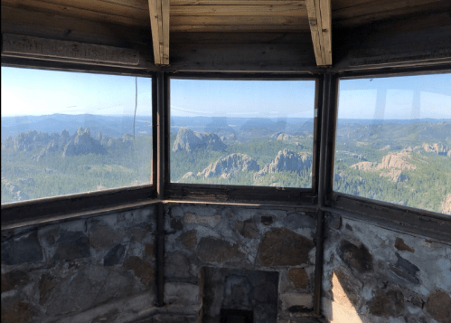 View from inside a stone lookout tower, showcasing a panoramic landscape of mountains and forests under a clear sky.
