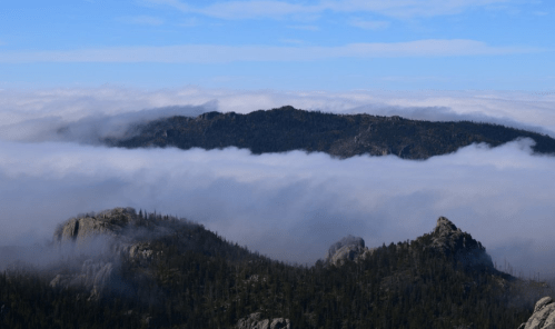 A scenic view of mountains rising above a sea of clouds under a clear blue sky.