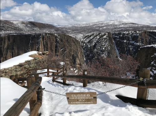 Snow-covered landscape with steep cliffs and a "Closed" sign warning of hazardous icy conditions.