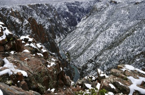 A snowy canyon with steep rock walls and a winding river at the bottom, surrounded by winter scenery.