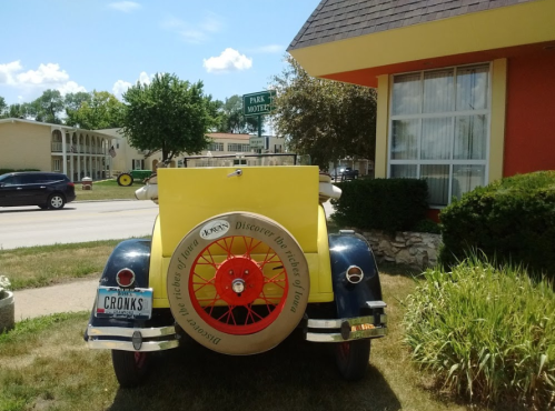A vintage yellow car parked outside a motel, with a sign reading "Park Motel" in the background.