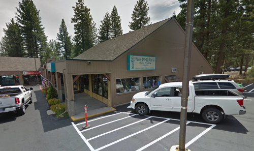 A building with a sign reading "The Outpost" surrounded by trees, with parked vehicles in front.