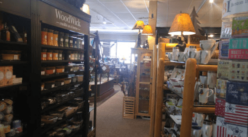 A cozy store aisle filled with candles, home goods, and decorative items, featuring wooden shelves and warm lighting.