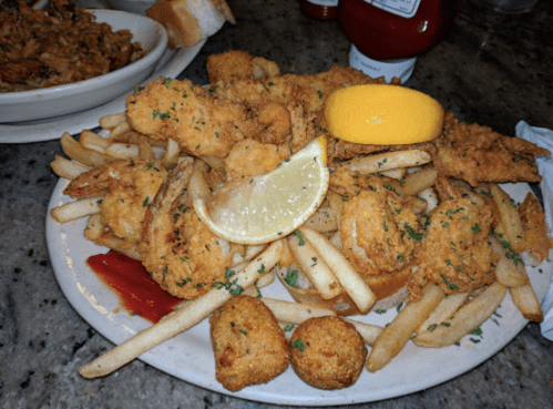A plate of fried shrimp, French fries, hushpuppies, and a lemon wedge, garnished with parsley and served with ketchup.