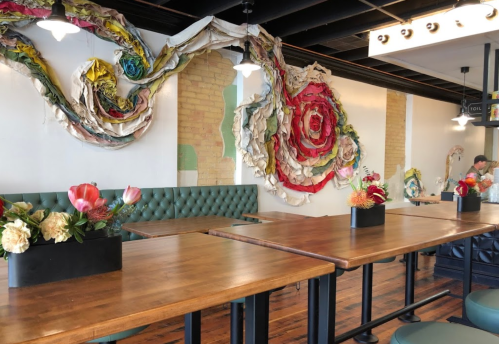 A cozy café interior featuring colorful wall art and floral centerpieces on wooden tables.