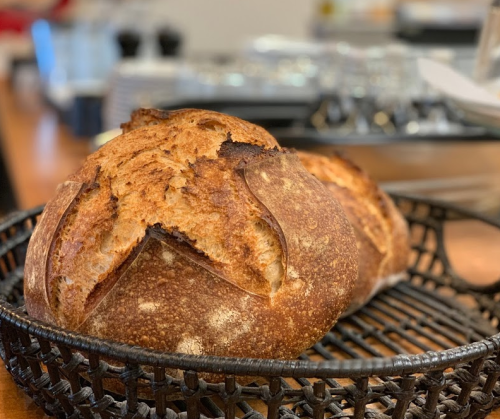 A close-up of two round loaves of freshly baked bread in a woven basket on a wooden table.