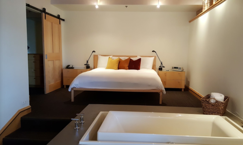 A modern bedroom featuring a large bed with colorful pillows, a stylish bathtub, and warm wooden accents.
