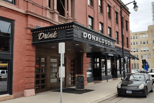 Exterior of a building with a sign reading "Donaldson" and "Drink," featuring a sidewalk and parked car.