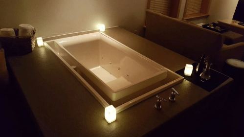 A modern, illuminated bathtub with candles around it, set in a cozy, dimly lit room.