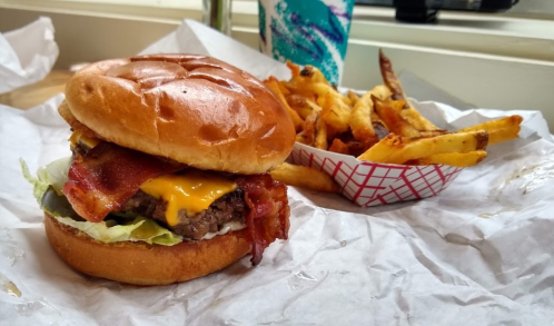 A juicy burger with bacon and cheese on a bun, served with a side of crispy fries in a paper container.