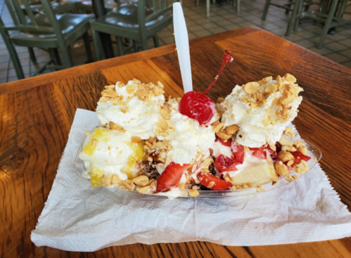 A colorful sundae with whipped cream, nuts, cherries, and fruit served in a dish on a wooden table.
