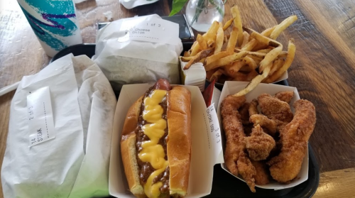 A tray with a hot dog topped with mustard, chicken tenders, fries, and two wrapped sandwiches.