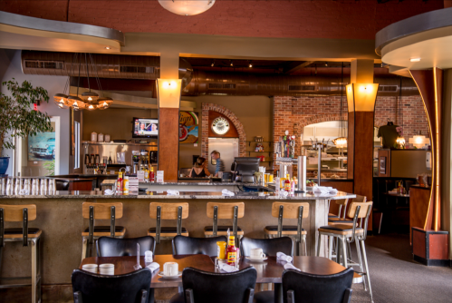 A cozy restaurant interior featuring a bar, tables, and staff preparing food in a warm, inviting atmosphere.