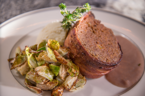 A plate featuring meatloaf, roasted Brussels sprouts, mashed potatoes, and a side of brown sauce.