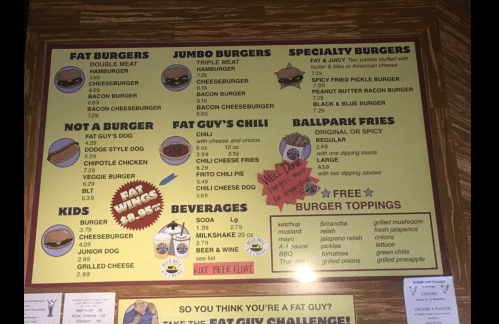 Menu board featuring various burgers, chili, hot dogs, fries, and beverages with playful graphics and descriptions.