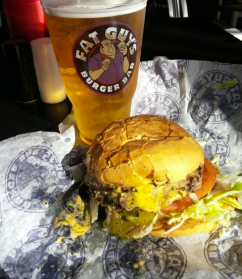 A juicy burger with melted cheese, lettuce, and tomato, served with a cold beer in a glass at a burger bar.