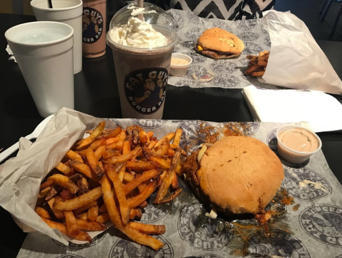 A table with a burger, fries, and a milkshake, all served in paper wrappers at a casual dining restaurant.