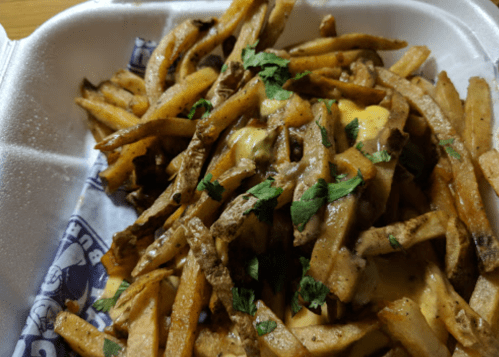 A close-up of a container filled with golden French fries topped with melted cheese and fresh cilantro.