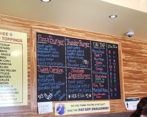 Menu board featuring various burgers, pizza options, and drinks, with prices listed for each item.