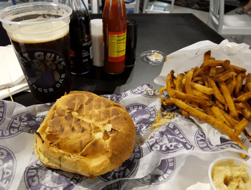A burger with a toasted bun, a side of crispy fries, and a glass of dark beer on a black table.