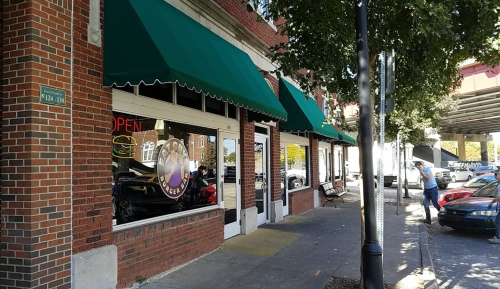 A street view of a restaurant with green awnings, an "Open" sign, and parked cars nearby.