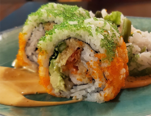 Close-up of colorful sushi rolls topped with green and orange fish roe, served on a blue plate with sauce.