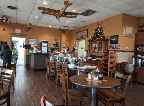 A cozy restaurant interior with wooden tables, chairs, and holiday decorations, featuring a buffet area and vintage airplane decor.
