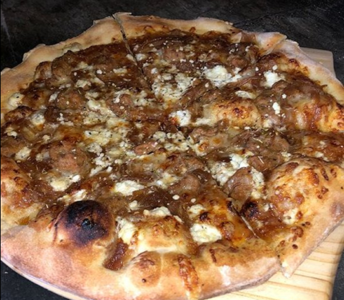 A freshly baked pizza topped with meatballs, cheese, and a golden crust, sliced and served on a wooden board.