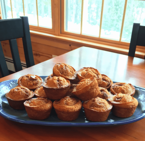 A blue platter filled with freshly baked muffins, arranged neatly, on a wooden table with large windows in the background.