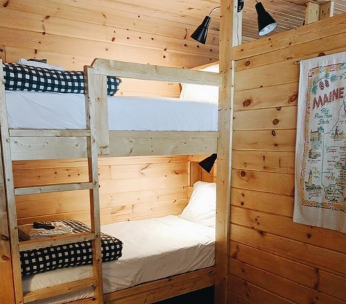 Cozy wooden bunk beds in a cabin, with checkered bedding and a wall hanging featuring a map of Maine.