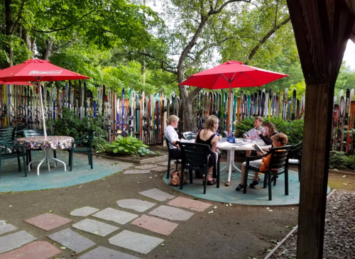 A group of people dining at a table under red umbrellas, surrounded by colorful ski decorations and greenery.