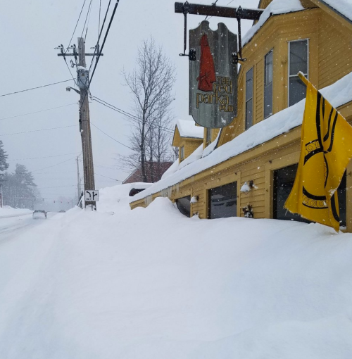 A snowy scene outside the Red Parka Pub, with heavy snow covering the ground and a flag waving in the wind.