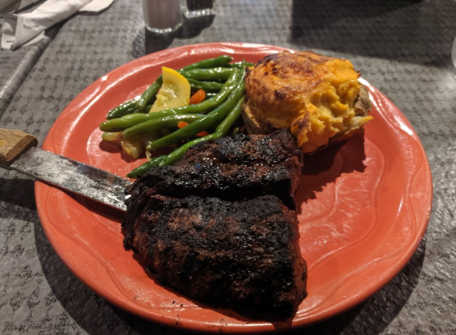 A plate with grilled steak, green beans, and a baked potato topped with cheese.