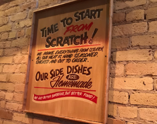A wooden sign on a brick wall promoting homemade food and hand-prepared meat dishes.