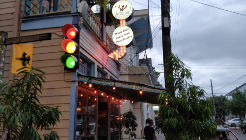 A colorful restaurant exterior with a sign reading "Warm Beer, Lousy Food, Poor Service" and a traffic light nearby.
