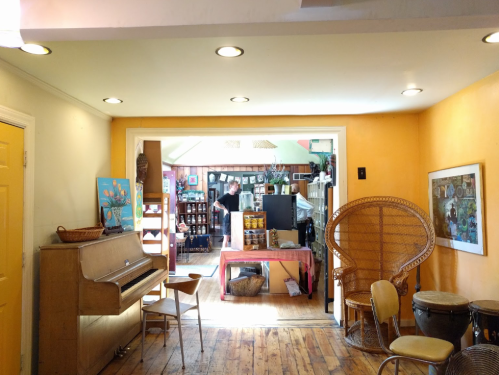 A cozy room with orange walls, a piano, a chair, and a view into a vibrant, cluttered space beyond.