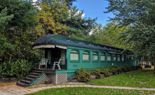 A vintage green train car converted into a cozy accommodation, surrounded by trees and greenery.
