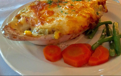 A baked dish with a golden cheese topping, served with green beans and sliced carrots on a white plate.