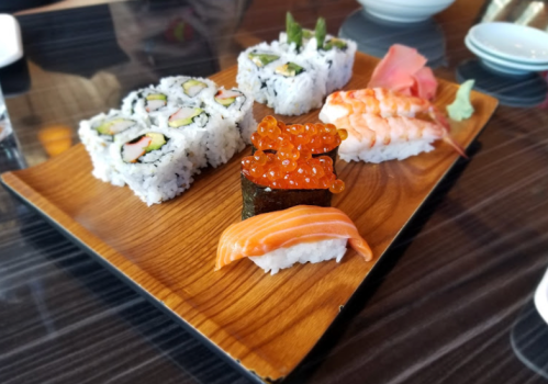 A wooden platter with various sushi pieces, including rolls, salmon, shrimp, and salmon roe.