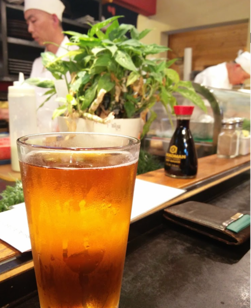 A glass of iced tea sits on a counter, with a chef and a potted plant in the background.