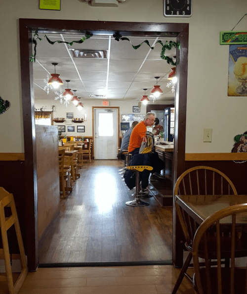 View through a doorway into a cozy restaurant, featuring wooden tables and patrons at the counter.