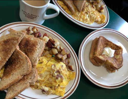 A breakfast spread featuring an omelet, toast, potatoes, and a slice of French toast with butter, alongside a coffee mug.