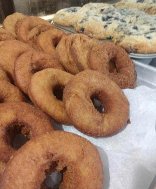 A tray of golden-brown donuts with a plate of blueberry scones in the background.