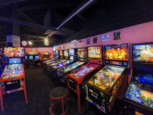 A vibrant arcade room filled with various pinball machines and colorful lights.