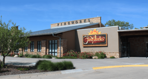 Exterior of a building with a sign reading "FireWorks," surrounded by greenery and a clear blue sky.