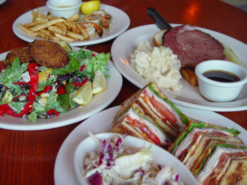 A table with a variety of dishes: a salad, fries, roast beef with mashed potatoes, and a layered sandwich.