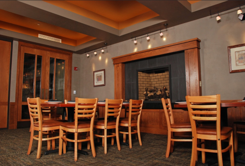Cozy restaurant interior featuring wooden tables, chairs, and a fireplace, with warm lighting and a welcoming atmosphere.