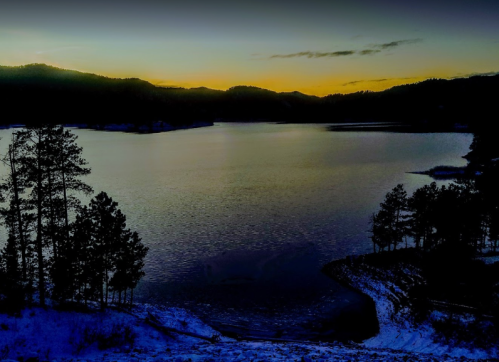 A serene lake at dusk, surrounded by mountains and silhouetted trees, reflecting soft twilight colors.