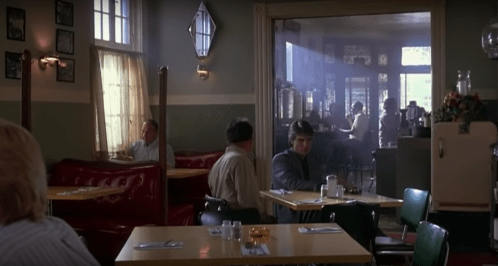 A dimly lit diner with red booths, tables, and patrons sitting quietly, creating a nostalgic atmosphere.